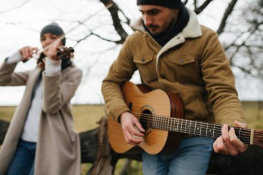 Yapraksız bir sonbahar ormanında müzik sanatını icra eden iki müzisyen.