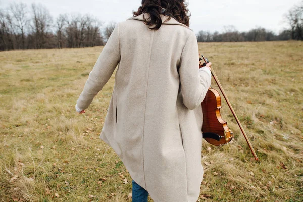 Varmt klädd kvinna går iväg med fiol på åkern på hösten — Stockfoto