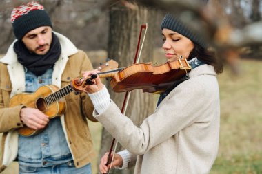 Sonbaharda kırsalda çalan, sıcak giyimli iki müzisyen.