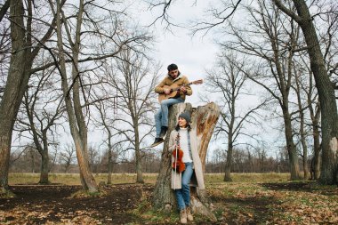 İki müzisyen güzel yapraksız bir sonbahar ormanında müzik çalıyorlar.