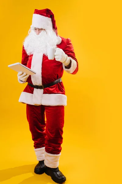 Santa pije z bílého hrnku čte něco — Stock fotografie
