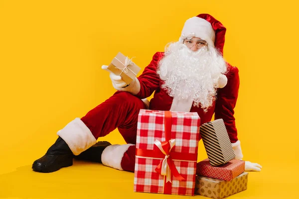 Retrato de Papai Noel sentado no chão no estúdio, segurando uma caixa na mão — Fotografia de Stock