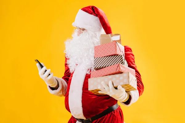 Papai Noel olhando para o telefone com muitos presentes em caixas — Fotografia de Stock