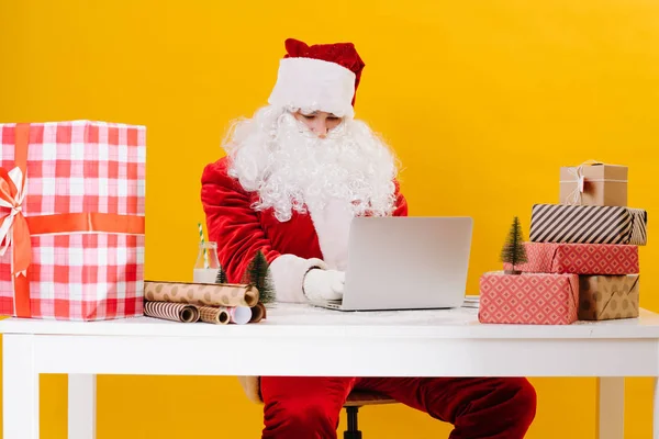 Santa Claus sedí u stolu, přijímá e-maily a připravuje vánoční dárky — Stock fotografie