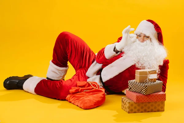 Papai Noel fica no chão e olha para a câmera enquanto segura óculos — Fotografia de Stock