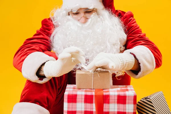 Papai Noel sentado no chão, cuidadosamente amarrando pequeno presente na frente dele — Fotografia de Stock