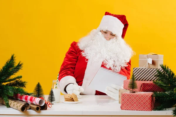 Santa Claus pracuje za stolem, kontroluje dárky a seznam adres — Stock fotografie