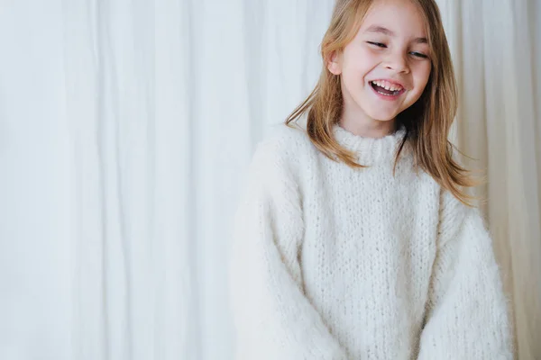 Feliz niña alegre en suéter de punto esponjoso blanco delante de una cortina —  Fotos de Stock