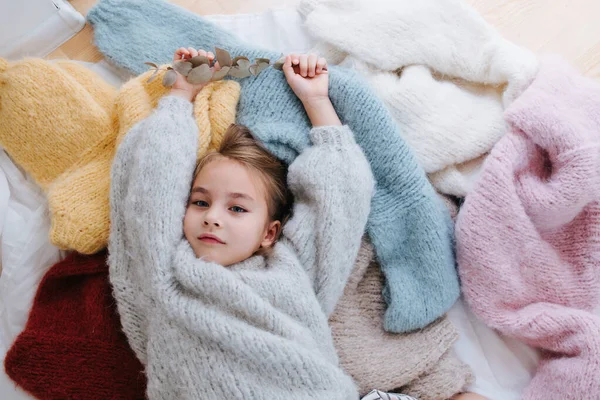 Petite fille endormie est couchée sur une pile de pulls multicolores doux — Photo