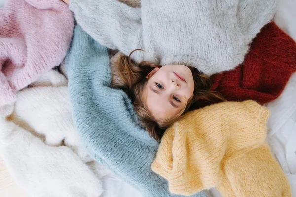 Schattig klein meisje ligt op een stapel zachte multi-gekleurde truien op de vloer. — Stockfoto