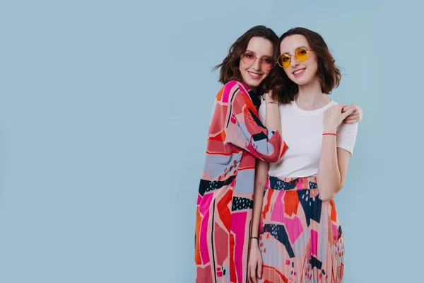 Cute portrait of twin sisters embracing, stand on a blue background — Stock Photo, Image