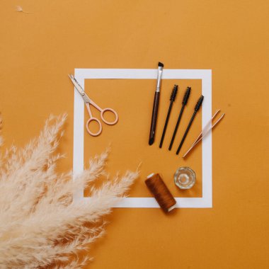 Turuncu arka planda kaş bakımını sağlayan aletlerin bileşimi. Üst görünüm