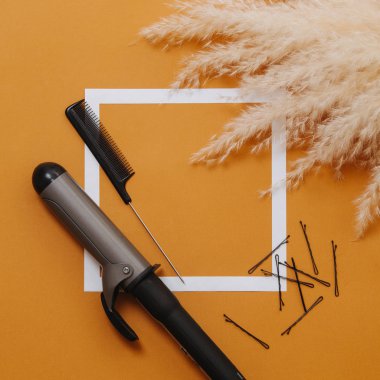 Saç maşası, fare kuyruğu tarağı ve turuncu arka planda tokalar. Üst görünüm