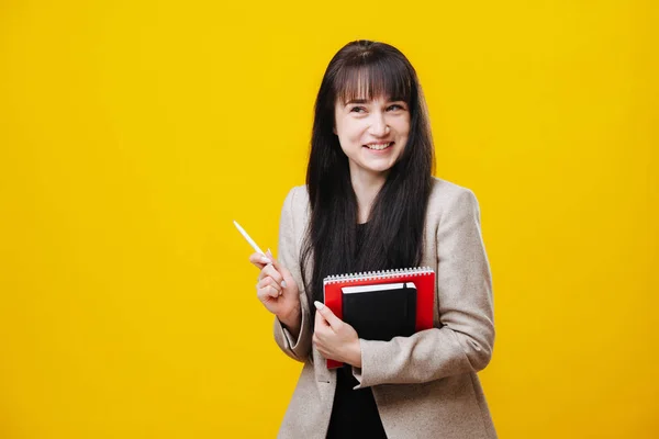 Χαμογελαστή νεαρή επιχειρηματίας με γκρι σακάκι κρατώντας στυλό πάνω από το κίτρινο — Φωτογραφία Αρχείου