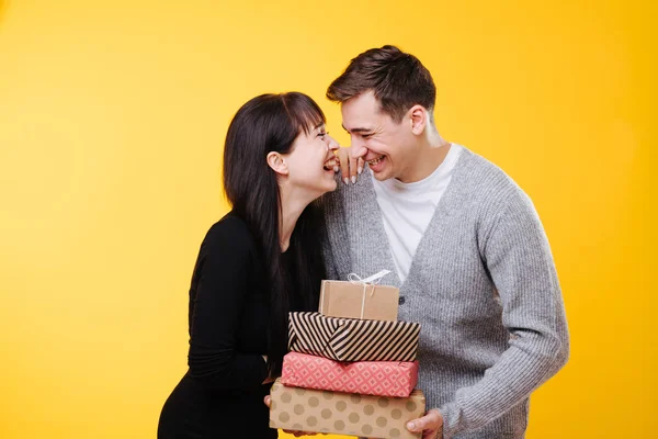 Feliz joven pareja riendo, mientras que el comercio de regalos sobre fondo amarillo — Foto de Stock