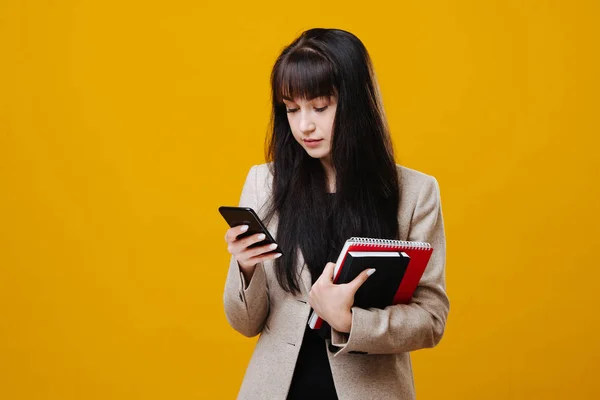 Jonge vermoeide zakenvrouw in een grijs pak controleren van haar telefoon over geel — Stockfoto