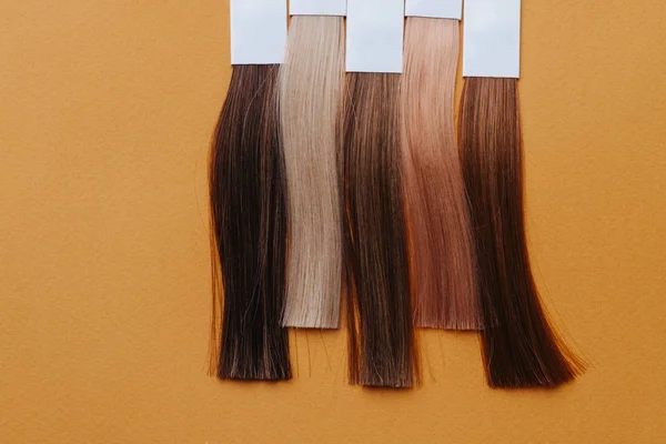 Vertical set of dyed hair locks. Samples in hairdressing salon on orange surface — Stock Photo, Image