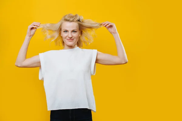 Playful grimacing blonde woman with hands on her waist over yellow — ストック写真
