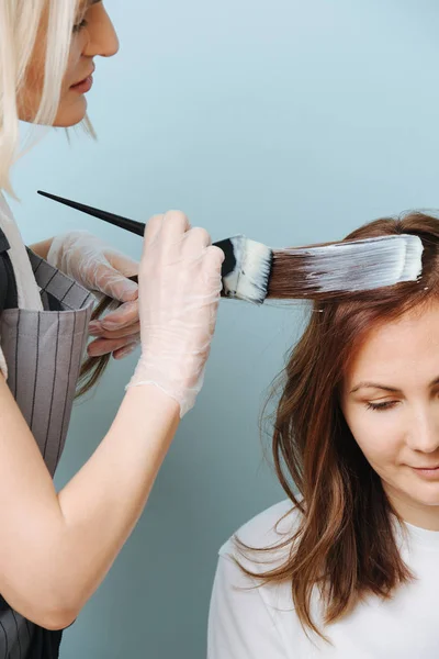 Cabeleireiro mulher loira aplicando desenvolvedor no cabelo do cliente sobre azul . — Fotografia de Stock