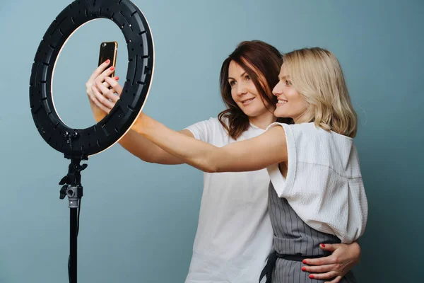 Estilista feminina está tomando selfie com um cliente com a ajuda de lâmpada de anel — Fotografia de Stock