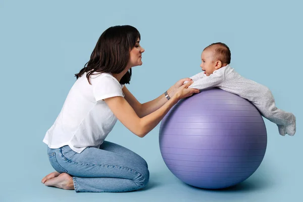 Young mother plays fitness ball with her baby. — Stock Photo, Image