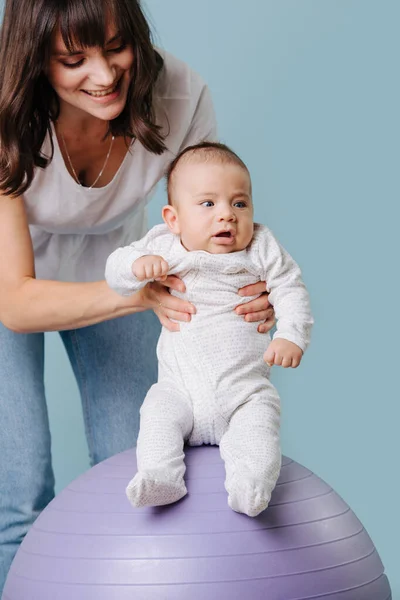 Mother does useful exercises by her infant son, on fitness ball — Stock Photo, Image