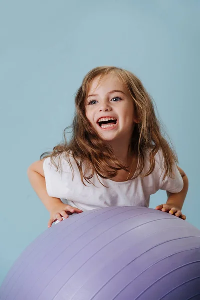 Blue-eyed girl plays with violet fintes ball. — Stock Photo, Image