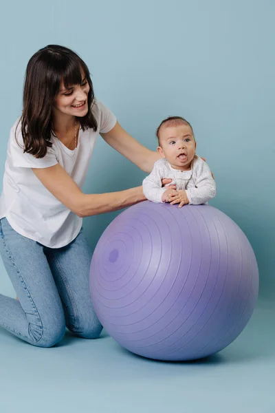 Young mom doing gymnastics with a baby on a lilac fitness ball — Stock Photo, Image