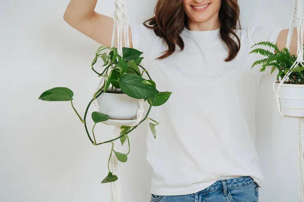 Woman holding pots with plans by a macrame pot-holders over white wall — Stockfoto