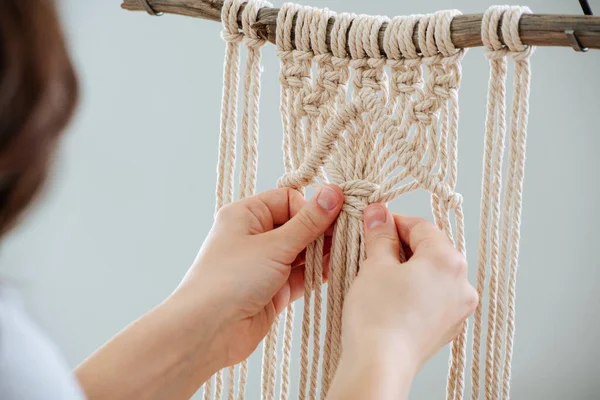 Craftswoman weving ropes, creating a macrame banner. from behind. Stockbild