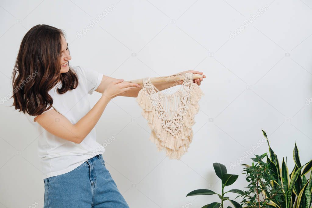 Laughing happy young woman holding an exquisite macrame piece over white wall