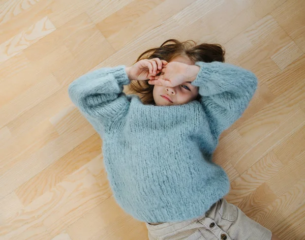 Sleepy little girl in a blue sweater waking up from napping on the floor — Stock Photo, Image