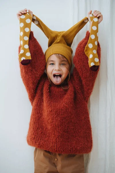 Grimacing naughty little girl in knitted sweater with tights on her head — Stock Photo, Image