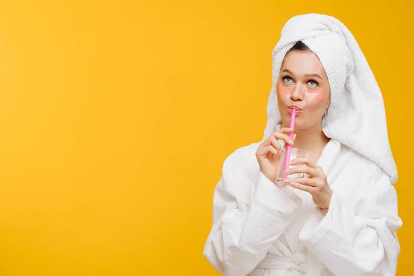 Mulher em roupão de banho com uma toalha na cabeça bebendo líquido de um copo com uma palha — Fotografia de Stock