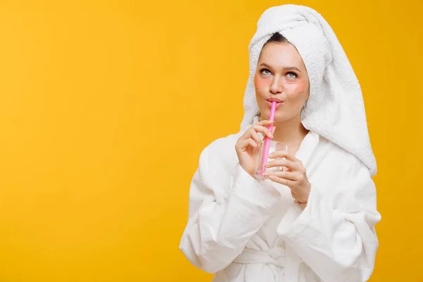 Vrouw in badjas met een handdoek op hoofd drinken vloeistof uit een glas met een rietje — Stockfoto