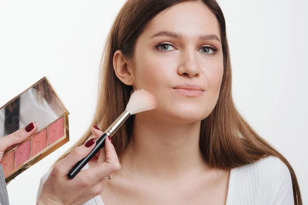 Mão com pincel aplicando blusher no rosto do cliente em uma sala brilhante — Fotografia de Stock