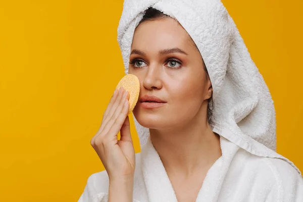 Middle-aged housewife applying moisturiser to her cheeks over yellow background. — Stock Photo, Image