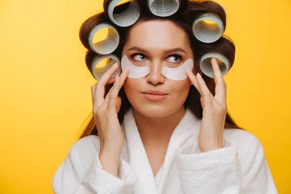 Woman in a beauty salon sits with hair in rollers holding patches to cheeks — Stock Photo, Image