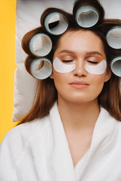 Jovem mulher cochilando no travesseiro com cabelo em rolos e manchas sob os olhos — Fotografia de Stock