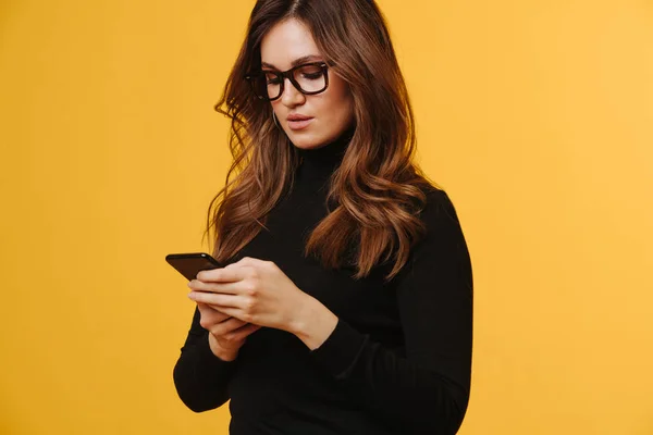 Brunette kvinne i svart, langt erme og briller som sms over gult – stockfoto
