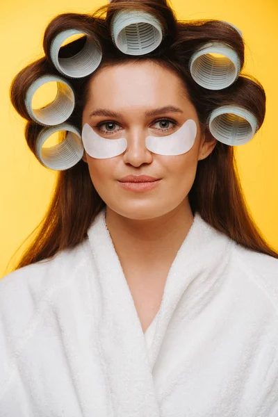 Middle aged woman in a beauty salon sits with hair in rollers and eye patches — Stock Photo, Image