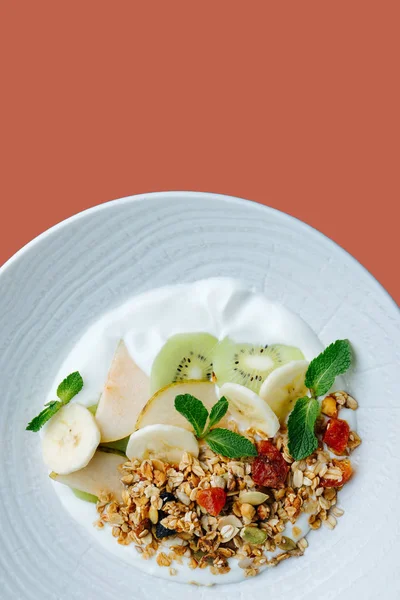 Muesli met gesneden vruchten, munt en zure room geserveerd op een wit bord — Stockfoto