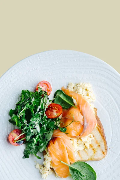 Salmone salato su pane tostato con insalata di spinaci e pomodoro servita su un piatto bianco — Foto Stock