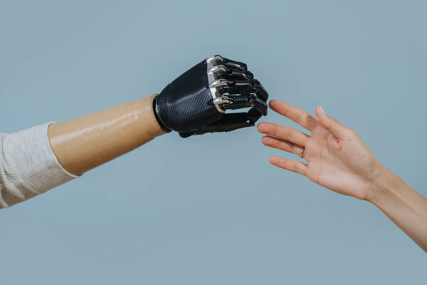 Two hands, living and bionic reaching for each other. Over blue background.