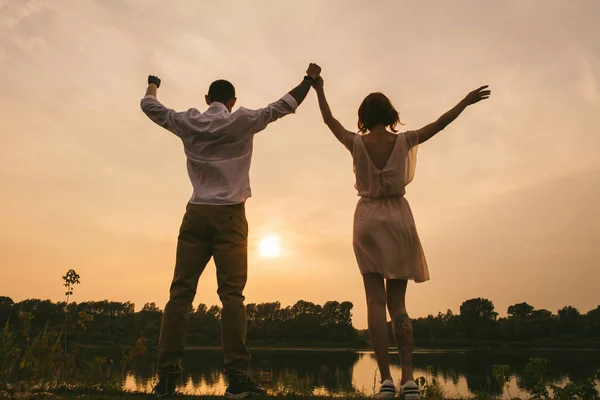 Couple debout sur un rivage de rivière, célébrant un beau coucher de soleil qui a lieu . — Photo