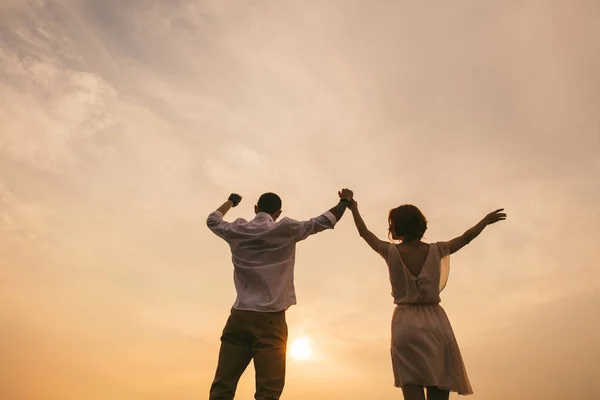 Coppia in piedi sotto un cielo arancione, guardando un bellissimo tramonto che si svolge . — Foto Stock