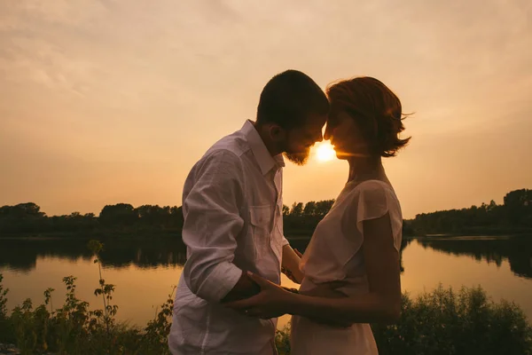 Par står på en flod strand, kyssas medan solen går ner — Stockfoto