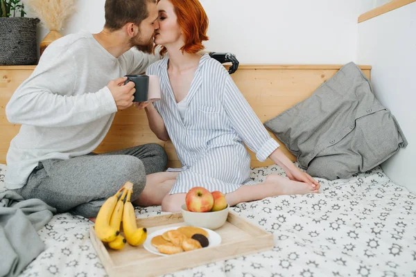 Feliz pareja de casados enamorados besándose en una cama doble en casa durante el desayuno — Foto de Stock