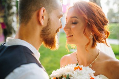 Gelin ve damat gün batımında parkta birbirlerine yakın duruyorlar.