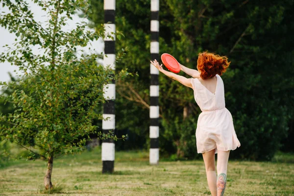 Kvinnan försöker fånga frisbee i en park på sommaren. Bakifrån. — Stockfoto